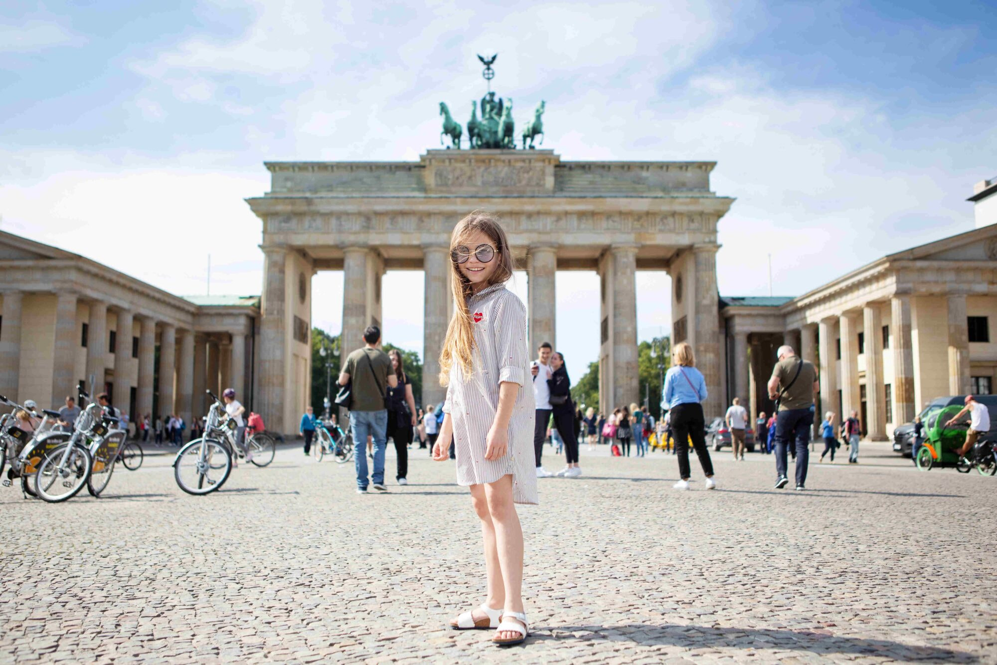Portrait of a little beautiful positive smiling stylish tourist girl near the Brandenburg Gate in Berlin in Germany.